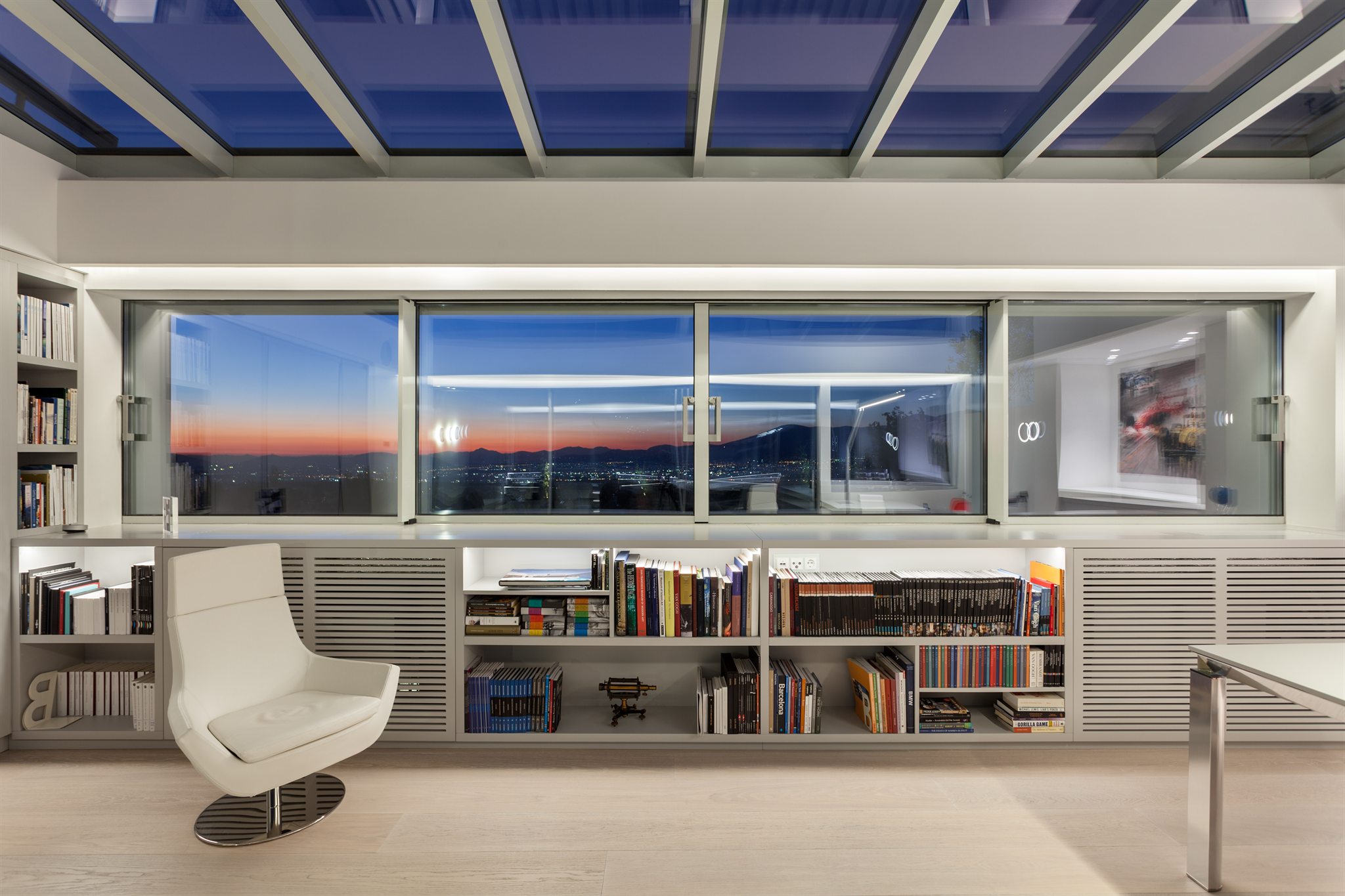 AKPRAXIS office interior at dusk with library shelving and a view over Athens — AKPRAXIS architecture and construction